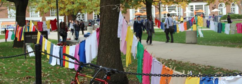 Clothes hanging on a clothesline at the quad with people walking by.