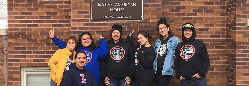 Group of six people smiling for the camera, standing outside the Native American House.
