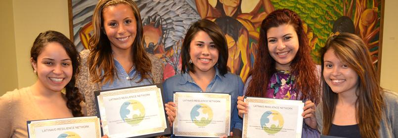 Five women standing side-by-side smiling, posing with certificates