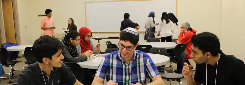 Students conversing at a table, with other students in the background
