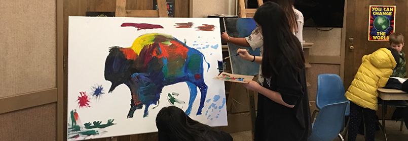 Picture of someone painting a colorful animal on a big canvas.
